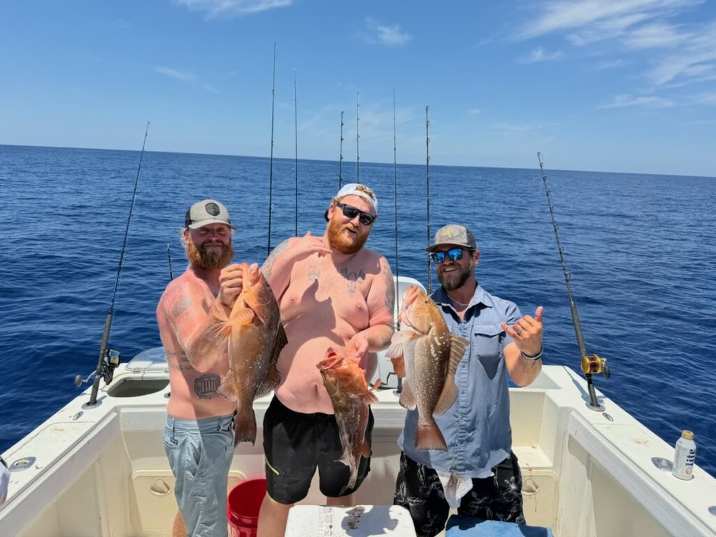 Three anglers on deck each holding a red grouper, flat calm Gulf behind them